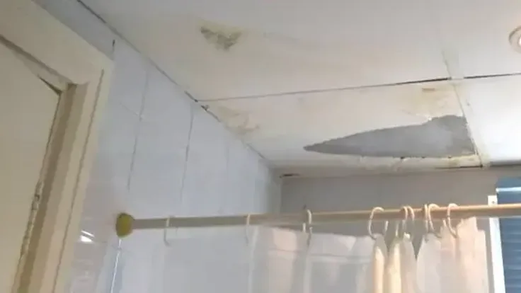 Water damage spreading across a bathroom ceiling above the shower