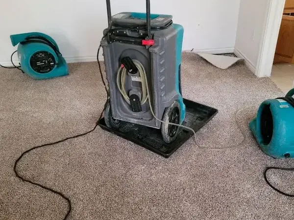 A dehumidifier and air movers drying bedroom carpet after a leak