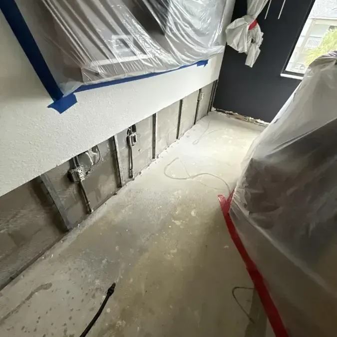 Plastic containment and flood-cut walls in a narrow room during drying