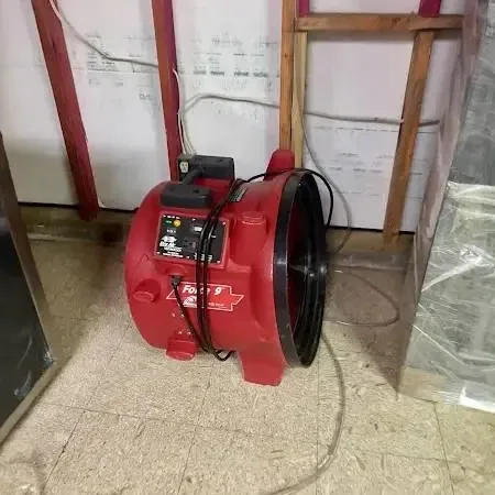 A red air mover in a room with the lower wall opened and plastic sheeting hung