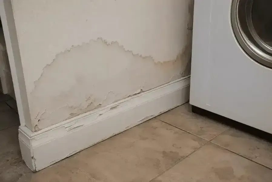 A stained wall and swollen baseboard next to a leaking washing machine